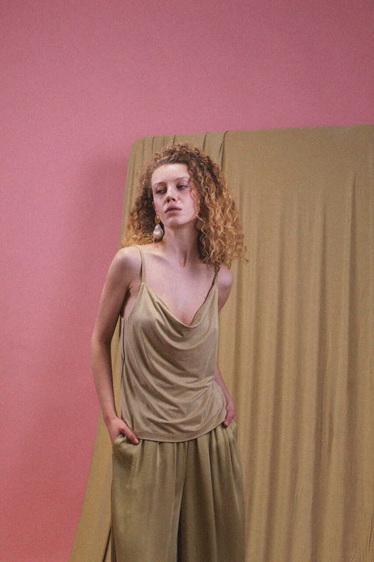 Cupro Drape Slip Top in Soft Olive worn by model against a pink backdrop, showcasing its draped neckline and fluid style.