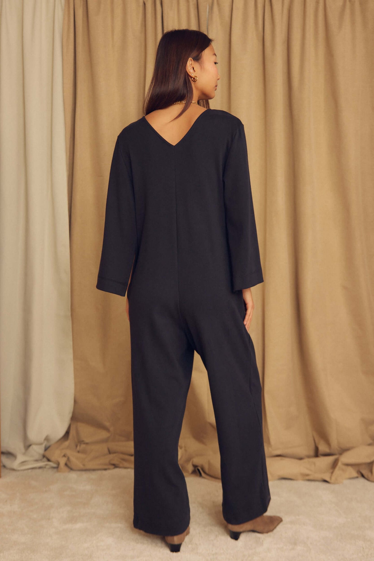 Woman wearing a Black Organic Cotton Wide-Leg Jumpsuit, showing the back and relaxed fit.