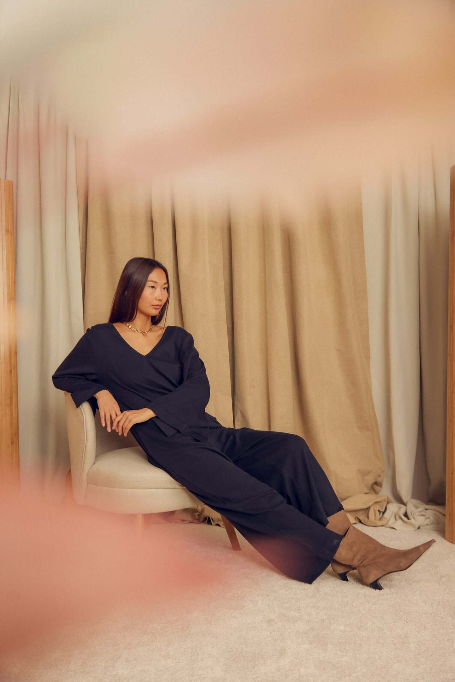 Model wearing a Black Organic Cotton Wide-Leg Jumpsuit sitting comfortably in a modern chair.
