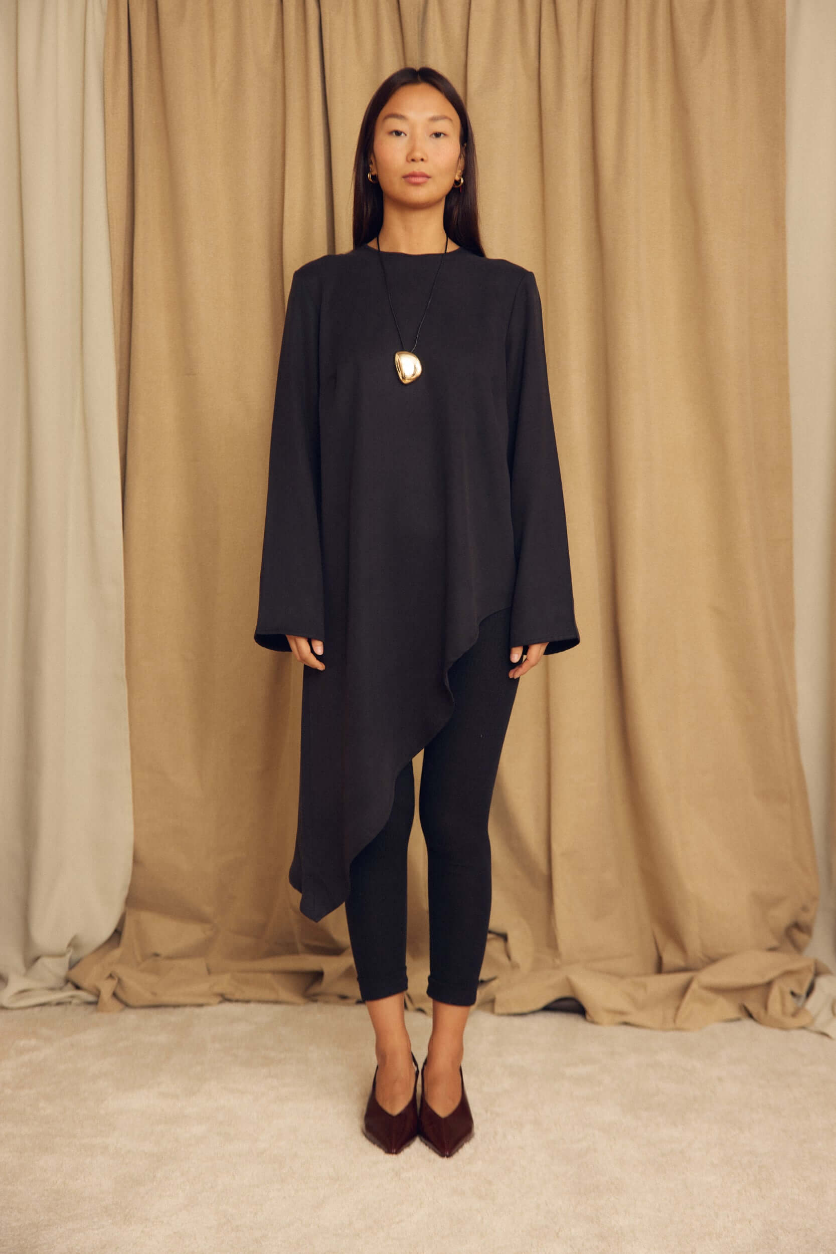 Model wearing a Black Lyocell Asymmetric Tunic with dramatic flared shape and asymmetric hemline.