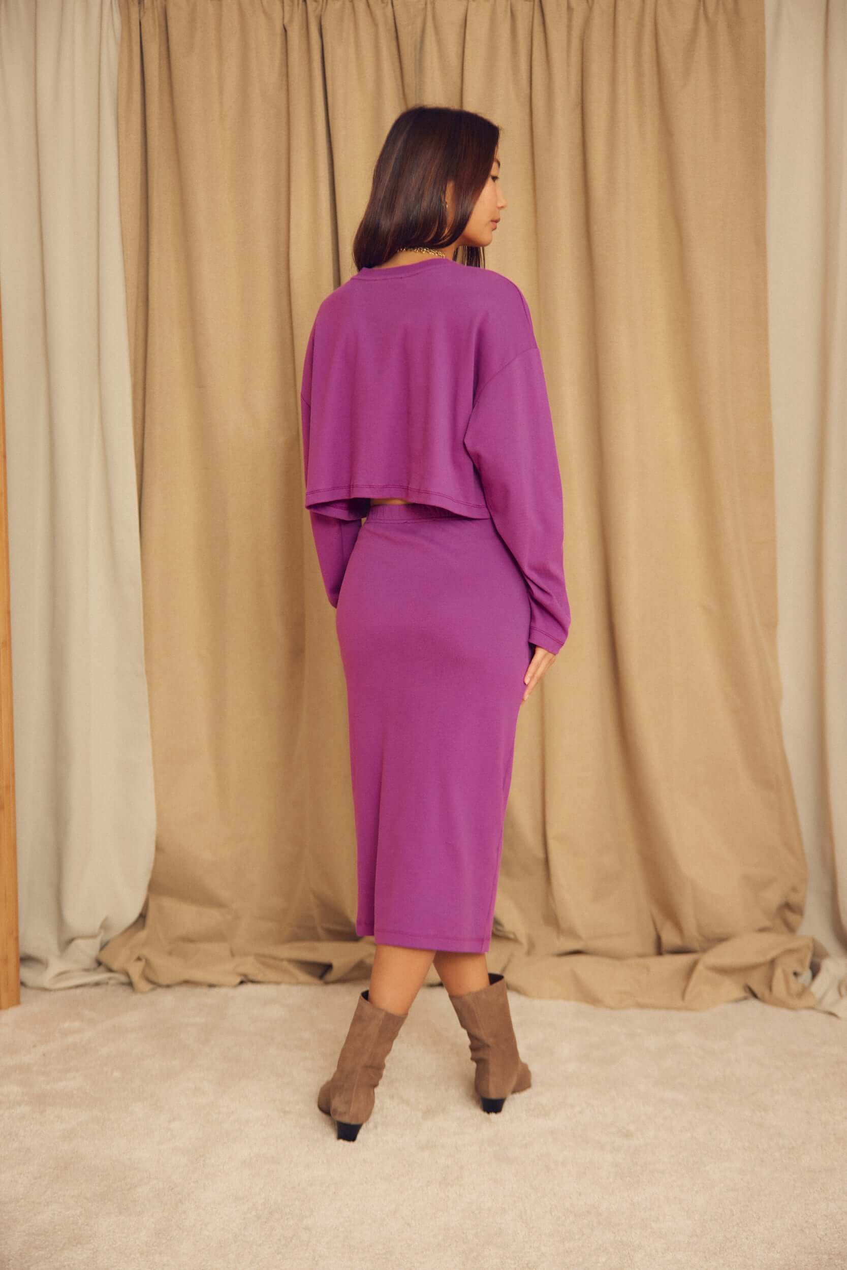 Model wearing a purple outfit featuring the Plum Organic Cotton Pencil Midi Skirt from the back.