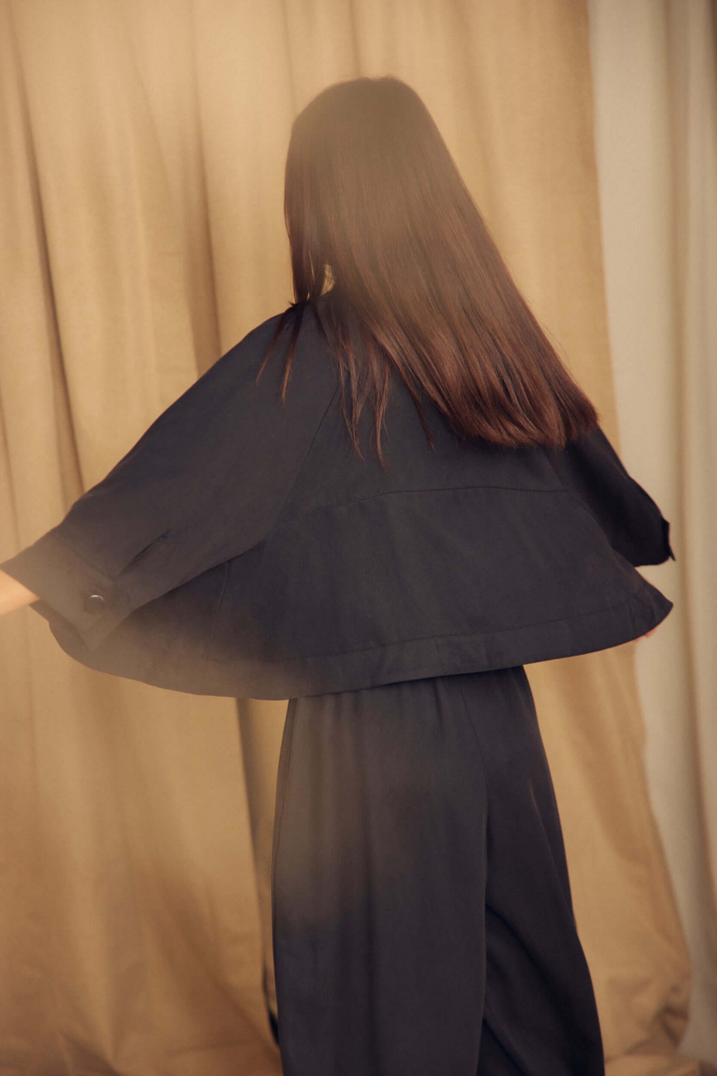 Back view of a model wearing the Black Lyocell Flared Jacket, showcasing its elegant flared silhouette.