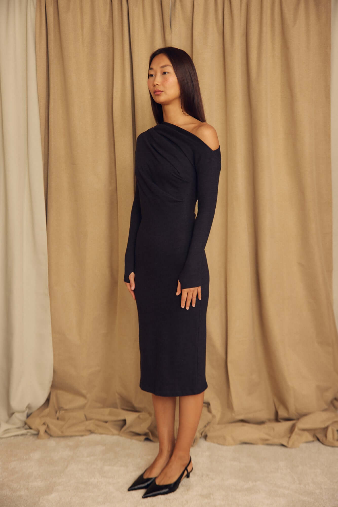 Model showcasing the Black Wool Drape Midi Dress with elegant neckline and fluid silhouette.