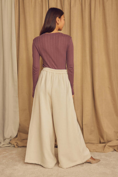 Model wearing Cocoa Lyocell Ribbed Long Sleeve Top with cream wide-leg pants, showcasing a relaxed back view.