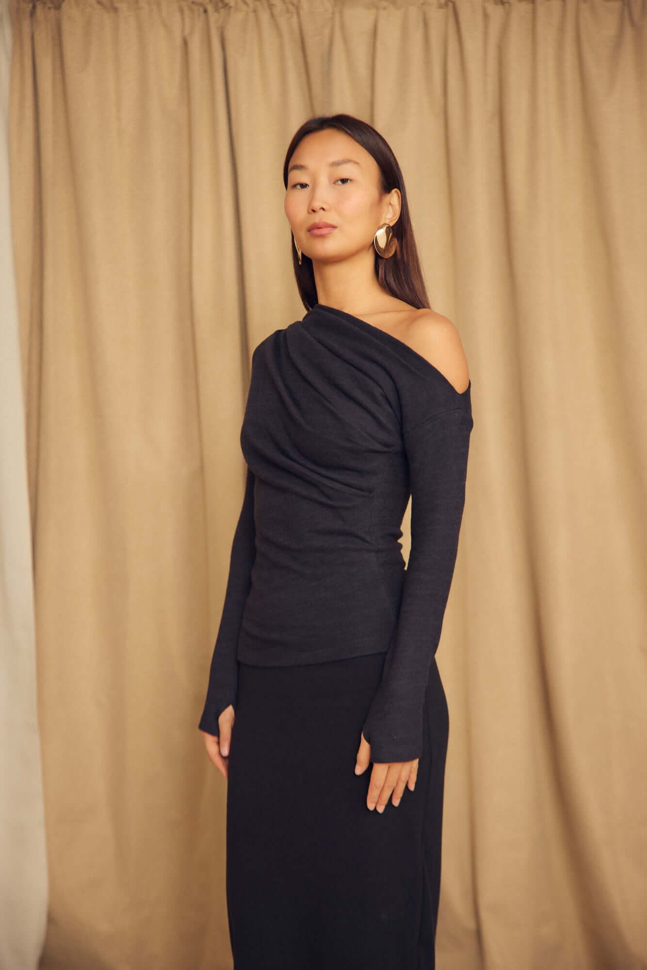 Black Wool Drape Top with Thumb Holes shown on a model, featuring an elegant draped neckline and fitted silhouette.