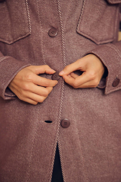 Close-up of hands buttoning Cocoa Organic Cotton Shacket, showcasing textured fabric and stylish design.