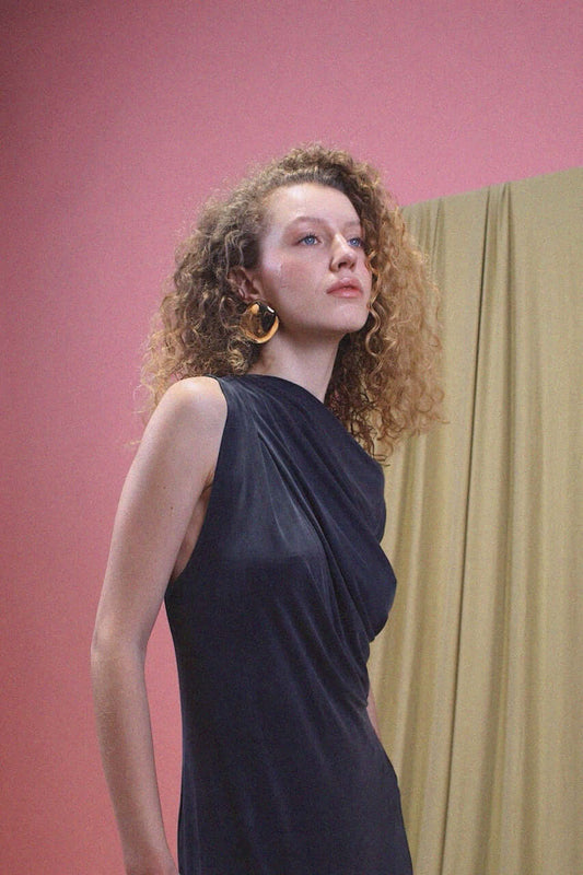Model showcasing the Drape Cupro Midi Dress in Slate Black against a pink and beige background.