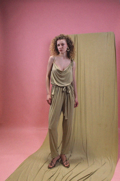 Model wearing a Cupro Slip Jumpsuit with Belt in Olive against a pink backdrop.