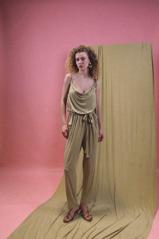 Model wearing a Cupro Slip Jumpsuit with Belt in Olive against a pink backdrop.