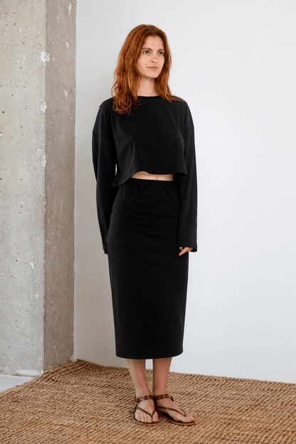 Model wearing Organic Cotton Midi Skirt in Black with matching cropped top, in a minimalist interior setting.