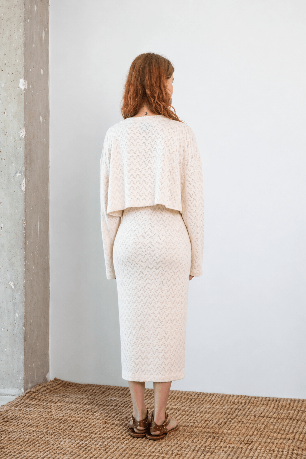 Model wearing Crochet Organic Cotton Midi Skirt in ecru from the back, showcasing its textured design and elegant silhouette.