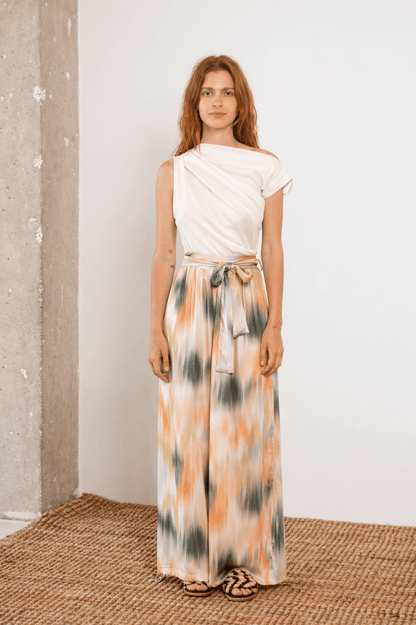 Model wearing a stylish outfit with a draped top and patterned maxi skirt, showcasing trendy summer fashion.