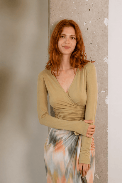 Image of a woman wearing the Cupro Multiway Wrap Top in Soft Olive, featuring a flattering wrap design and thumb hole detailing.