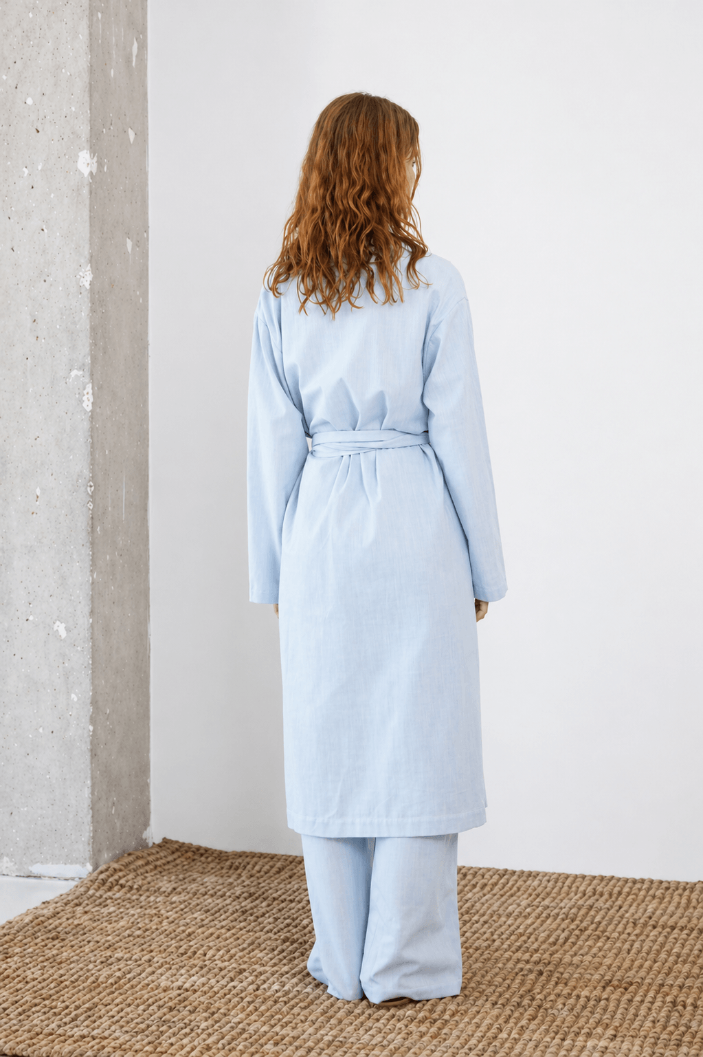 Lightweight Organic Cotton Trench Coat in Pale Blue worn by model from the back, featuring a relaxed silhouette and detachable belt.