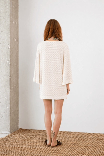 Back view of a model wearing an Organic Cotton Crochet Mini Dress in ecru with flared sleeves.