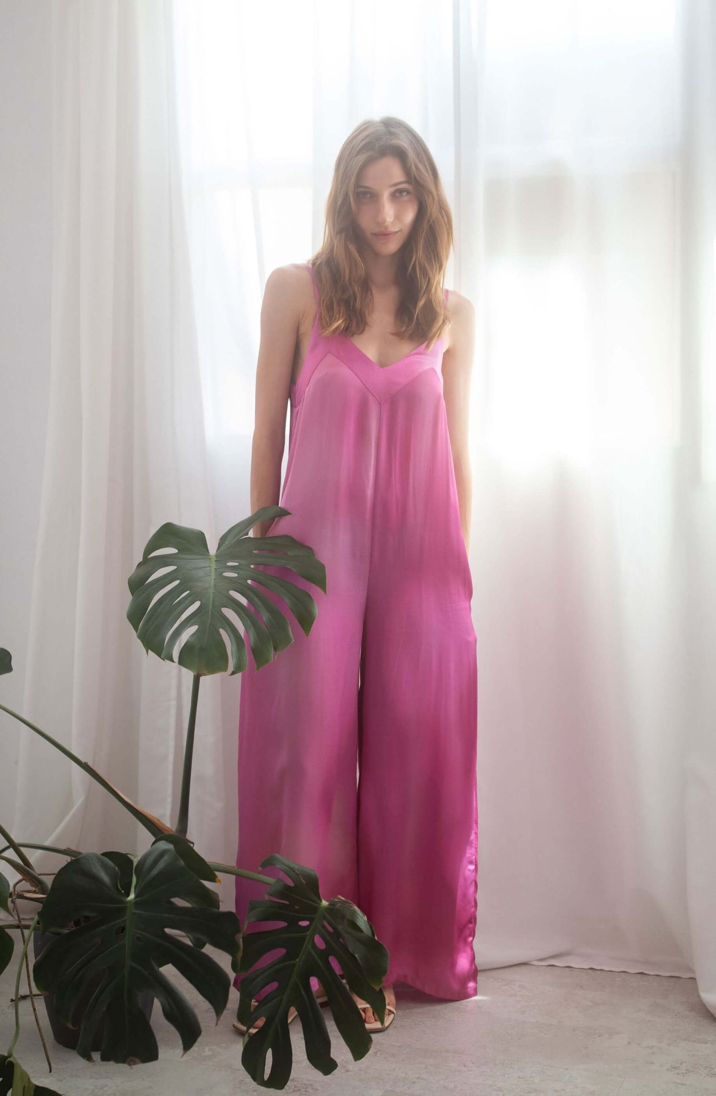 PRINT WIDE JUMPSUIT worn by model with side pockets and adjustable straps, in vibrant pink, set in airy room.