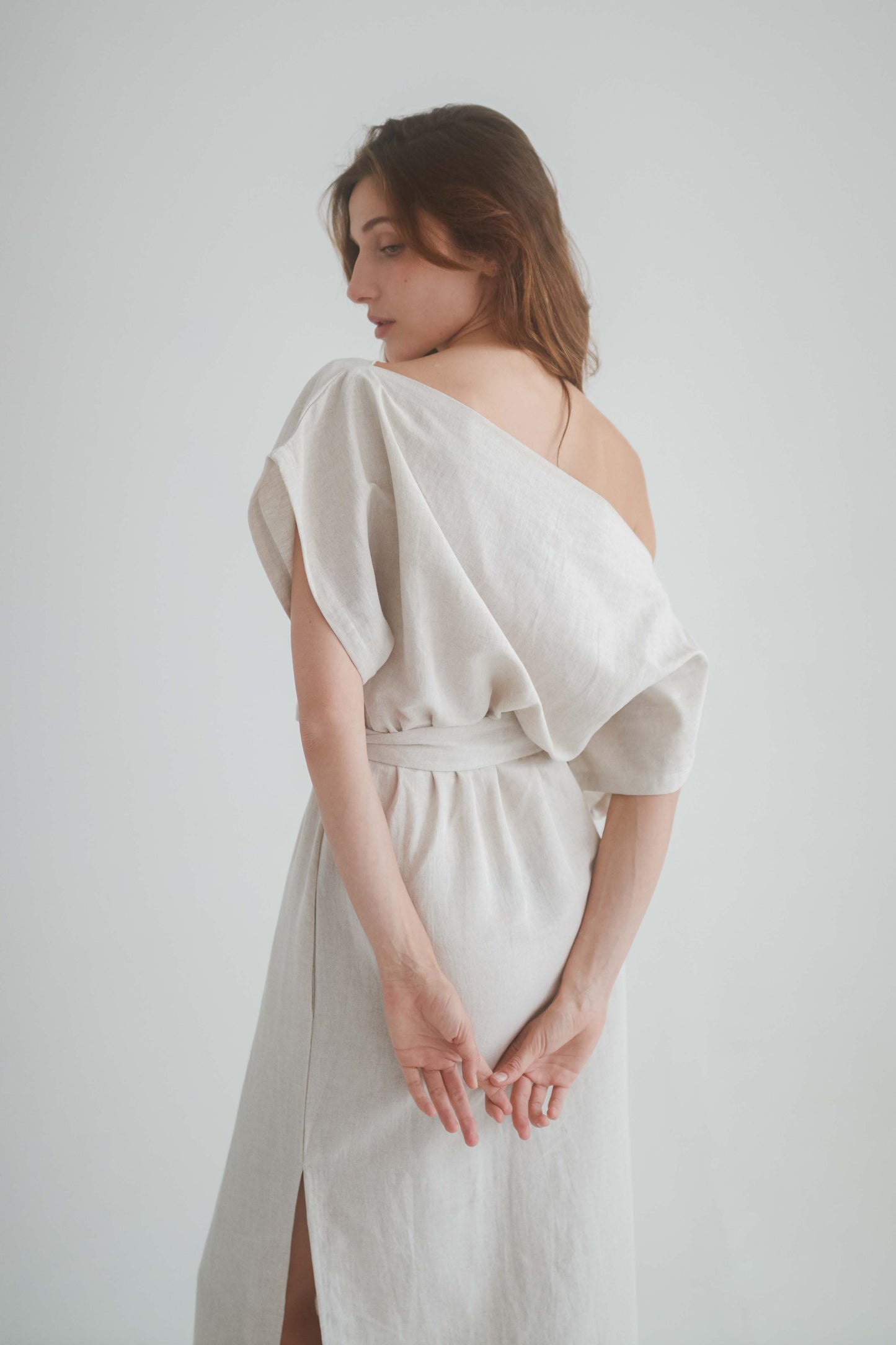 Back view of a model in a natural drape dress featuring an off-shoulder neckline and elasticated waist.