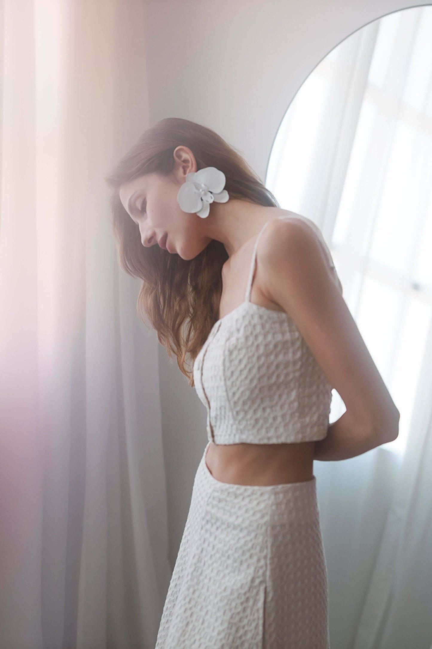 Model wearing ECRU WAFFLE CROP TOP with adjustable straps and shirred back, styled with a floral earring.