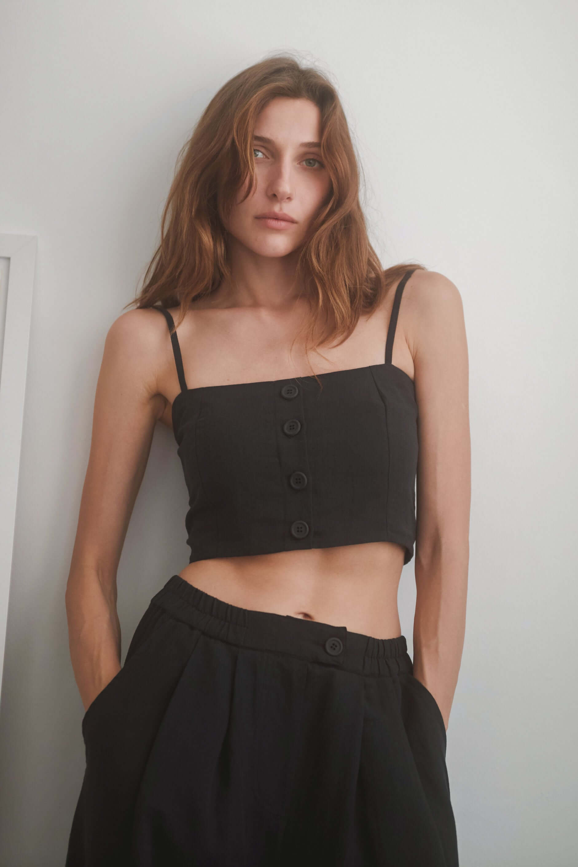 Black crop top with eco-friendly woven fabric, adjustable straps, and eco buttons, styled with matching wide trousers.