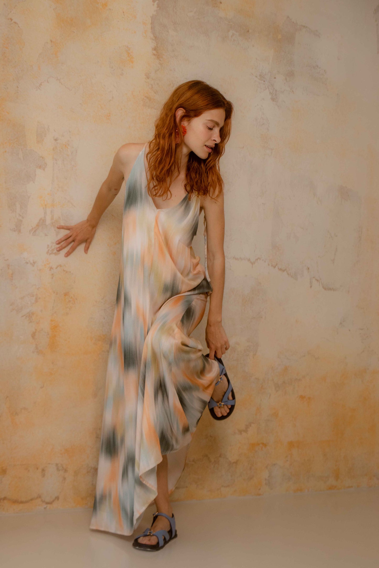 Model wearing a Printed Ecovero Viscose Maxi Dress against a textured wall, showcasing its fluid drape and colorful print.
