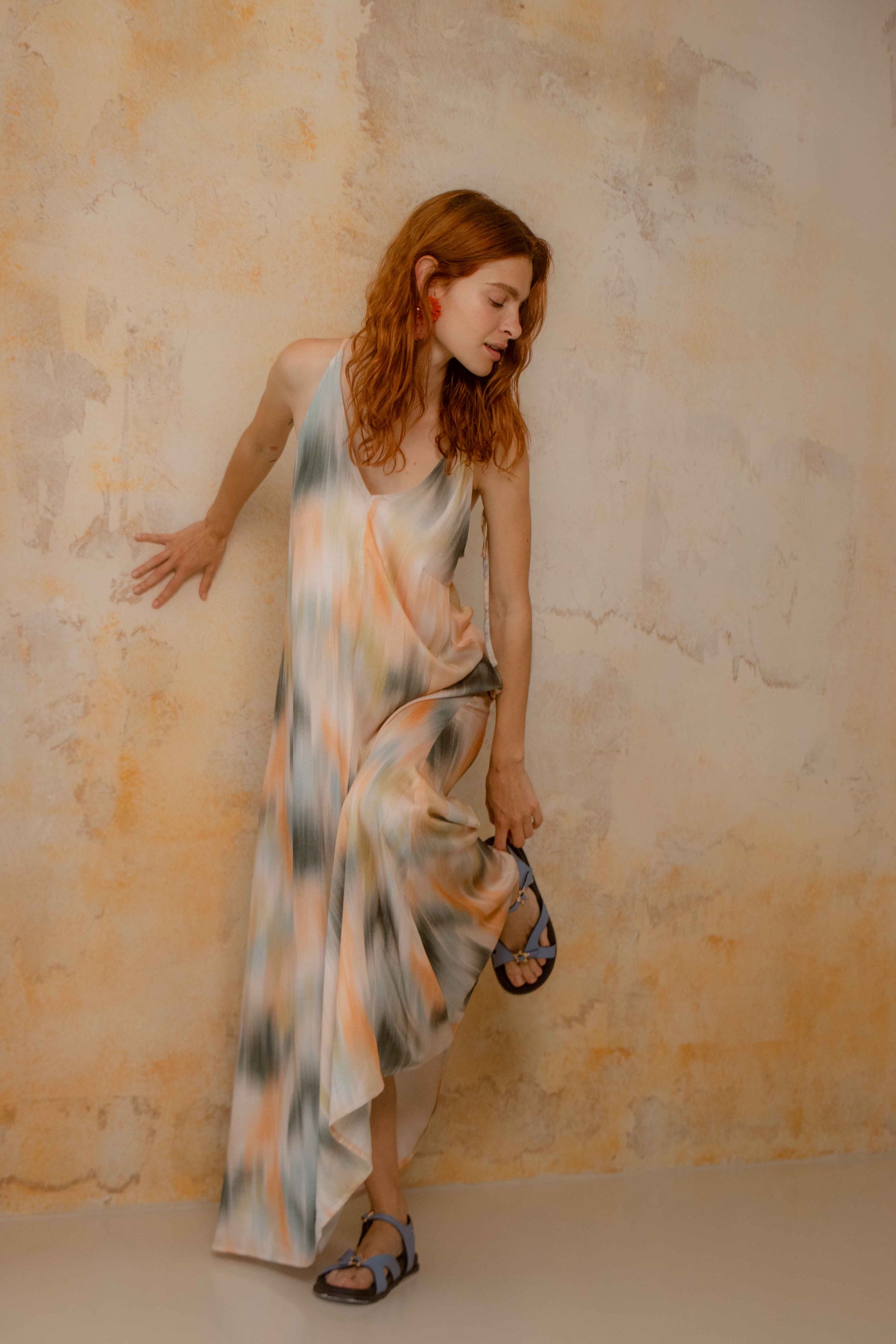Model wearing a Printed Ecovero Viscose Maxi Dress against a textured wall, showcasing its fluid drape and colorful print.