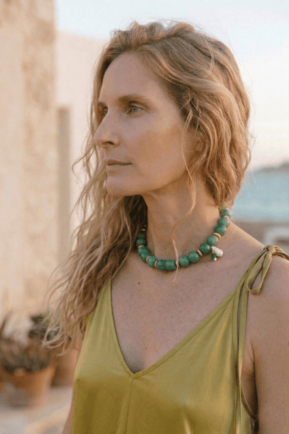 Ecovero Maxi Dress in Soft Olive worn by a woman with wavy hair and a green beaded necklace outdoors.