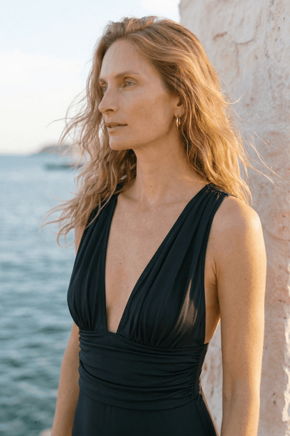 Gathered Neckline Swimsuit in Black worn by a woman near the water, showcasing its elegant silhouette and soft fabric.