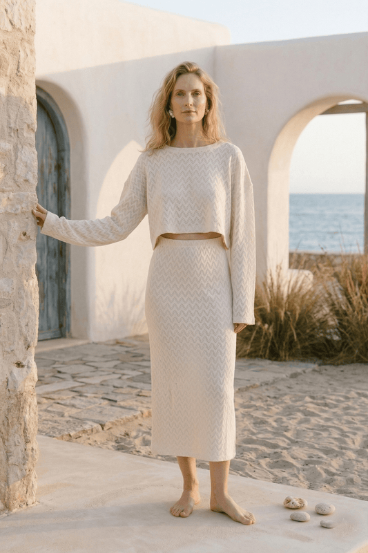 Model wearing a Crochet Organic Cotton Midi Skirt and matching top in ecru, with a beach background.