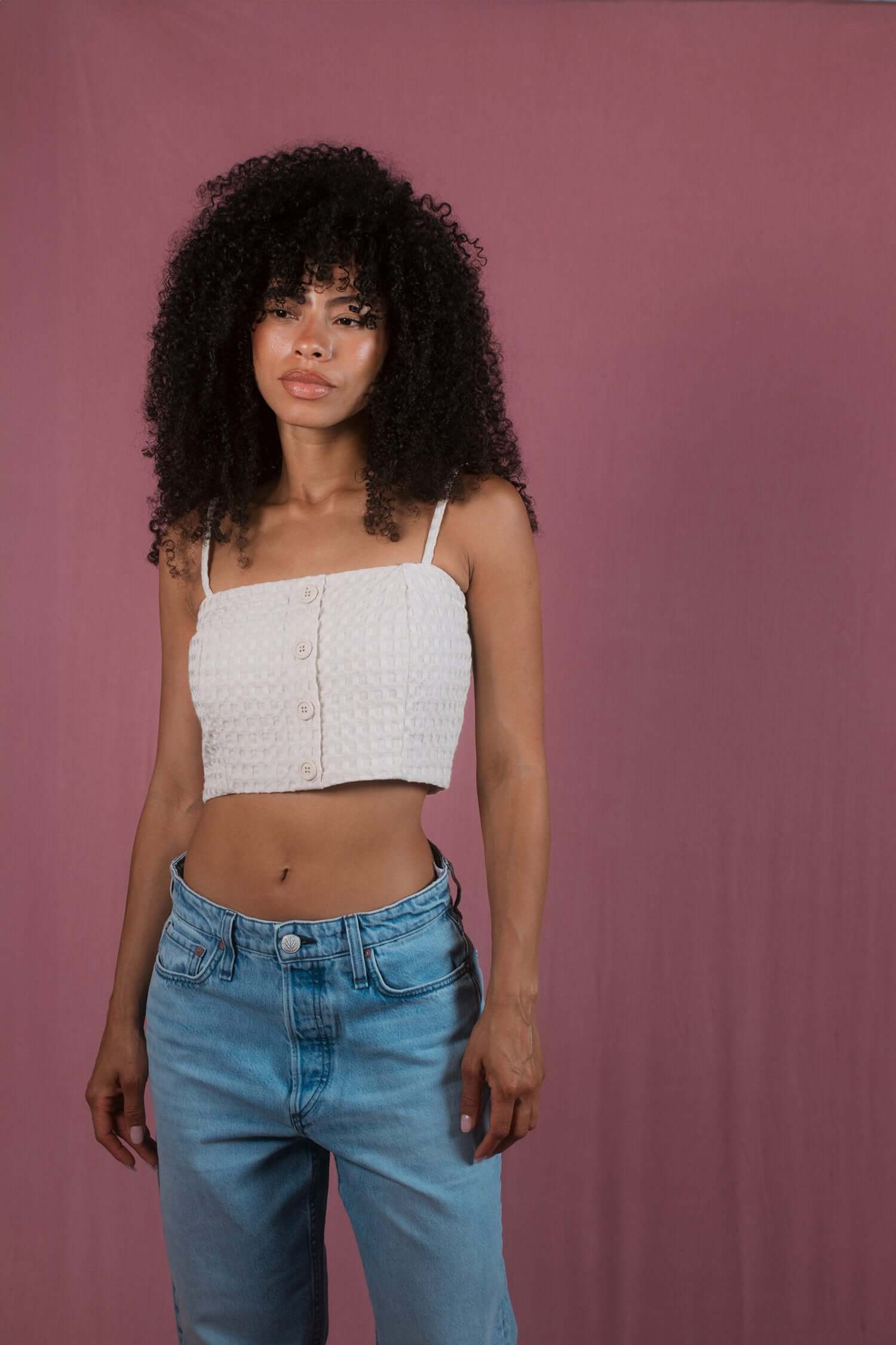 ECRU WAFFLE CROP TOP worn by a model with curly hair, styled with high-waisted jeans against a pastel background.