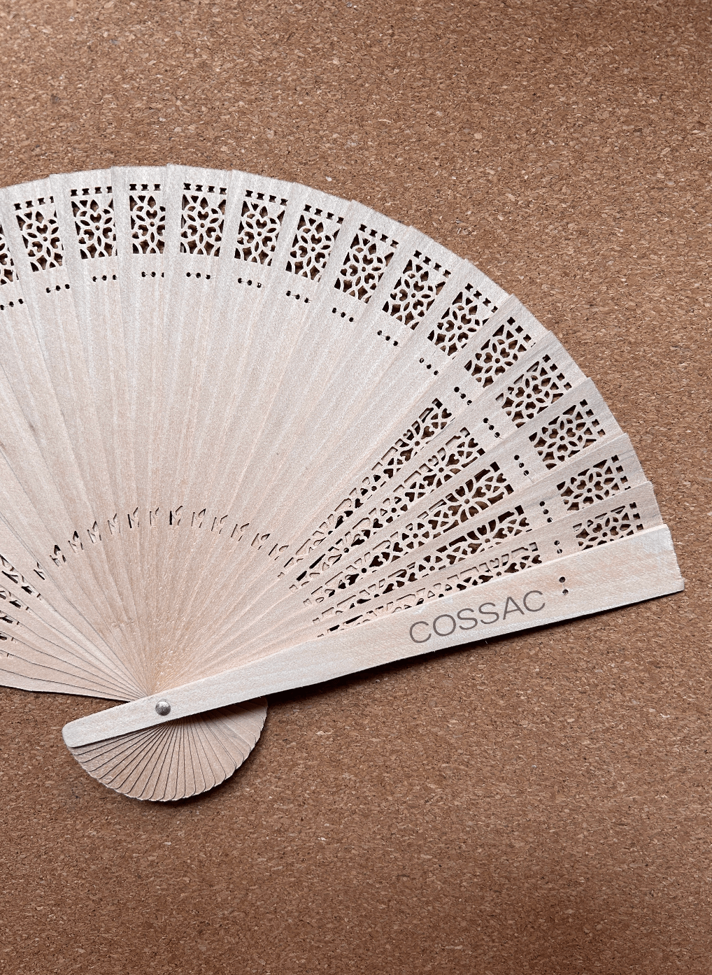 Wooden fan made of recycled Spanish wood, featuring intricate cutouts and 'COSSAC' logo, size 30x30cm.