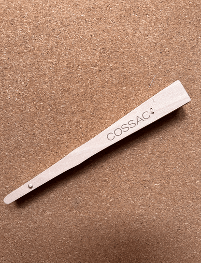 COSSAC branded wooden fan, made from recycled wood, showcasing minimalist design on a natural cork background.
