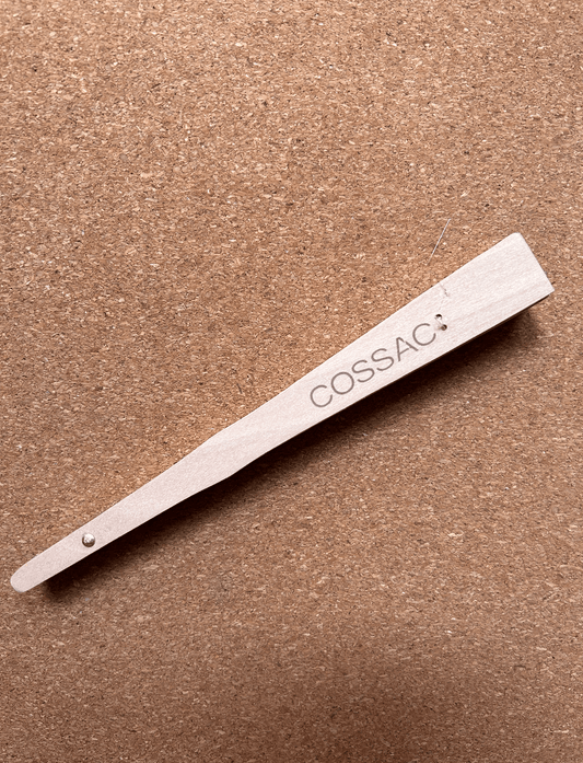 COSSAC branded wooden fan, made from recycled wood, showcasing minimalist design on a natural cork background.