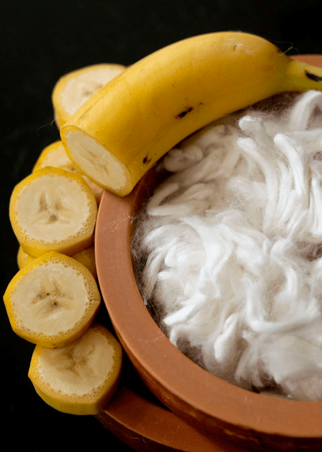 Banana Pineapple Multiway Wrap Top in Ecru surrounded by fresh bananas and textured fibers in a clay bowl.