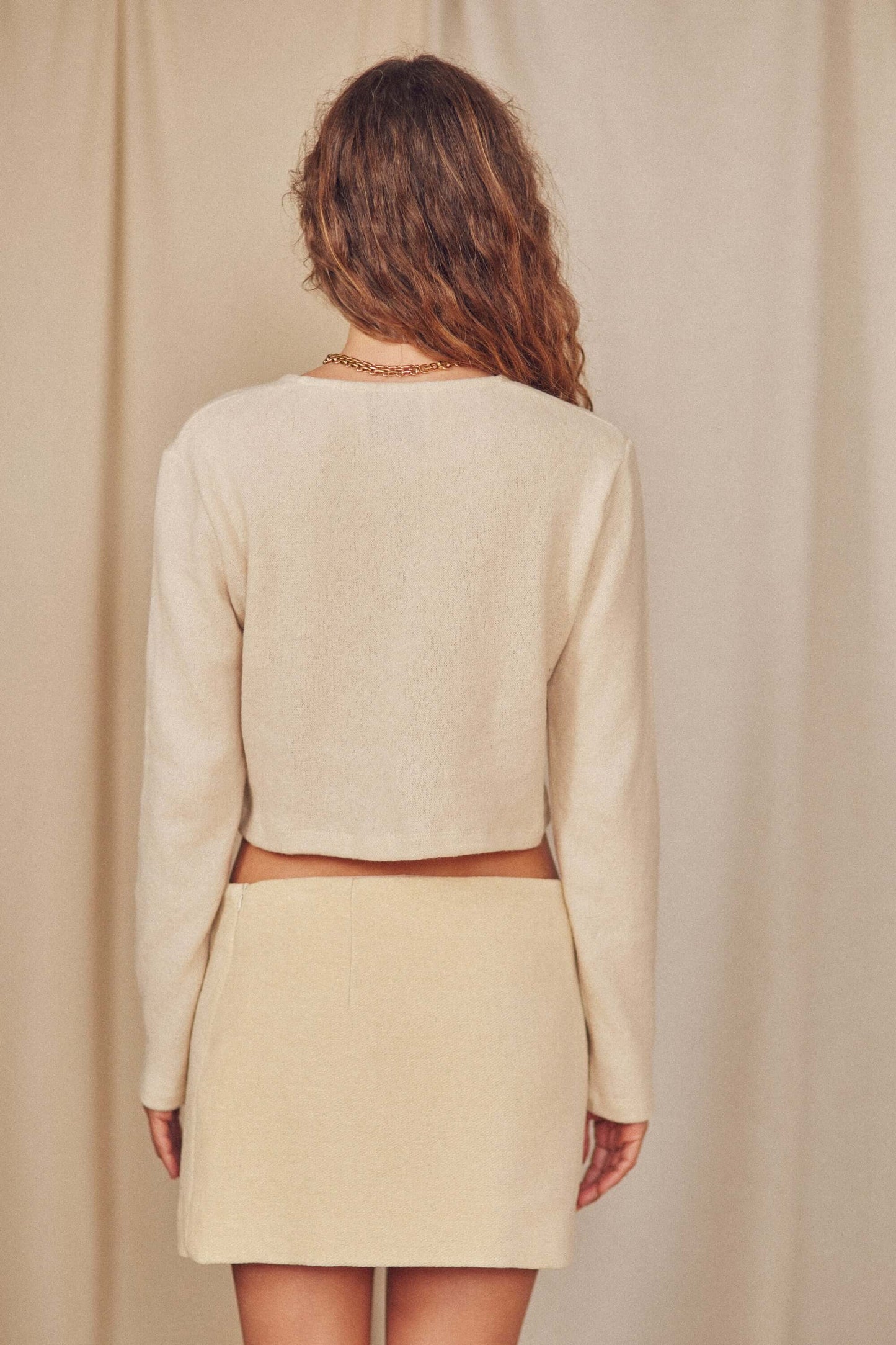 Back view of a model wearing an Oat Wool Crop Knit Cardigan paired with a mini skirt.
