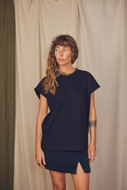 Model wearing a black organic cotton mini skirt with an elegant thigh split and relaxed black top.