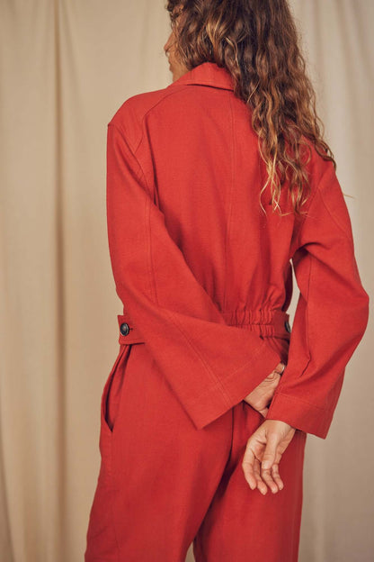 Back view of a woman wearing a Rust Organic Cotton Boiler Suit with a cinched waist and wide sleeves.