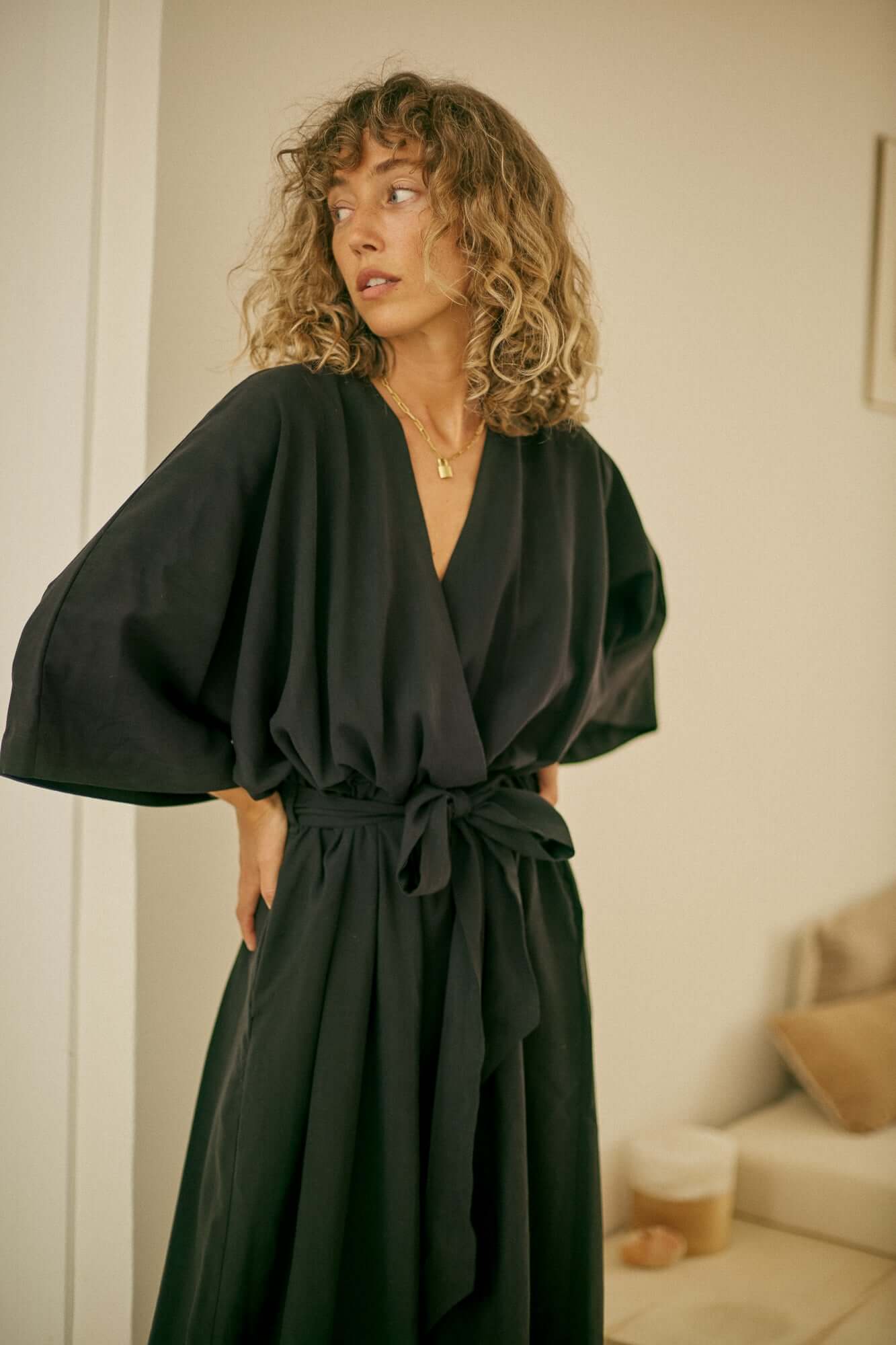 Tencel Kimono Jumpsuit in Black worn by a model with curly hair and a relaxed pose, showcasing its elegant silhouette.