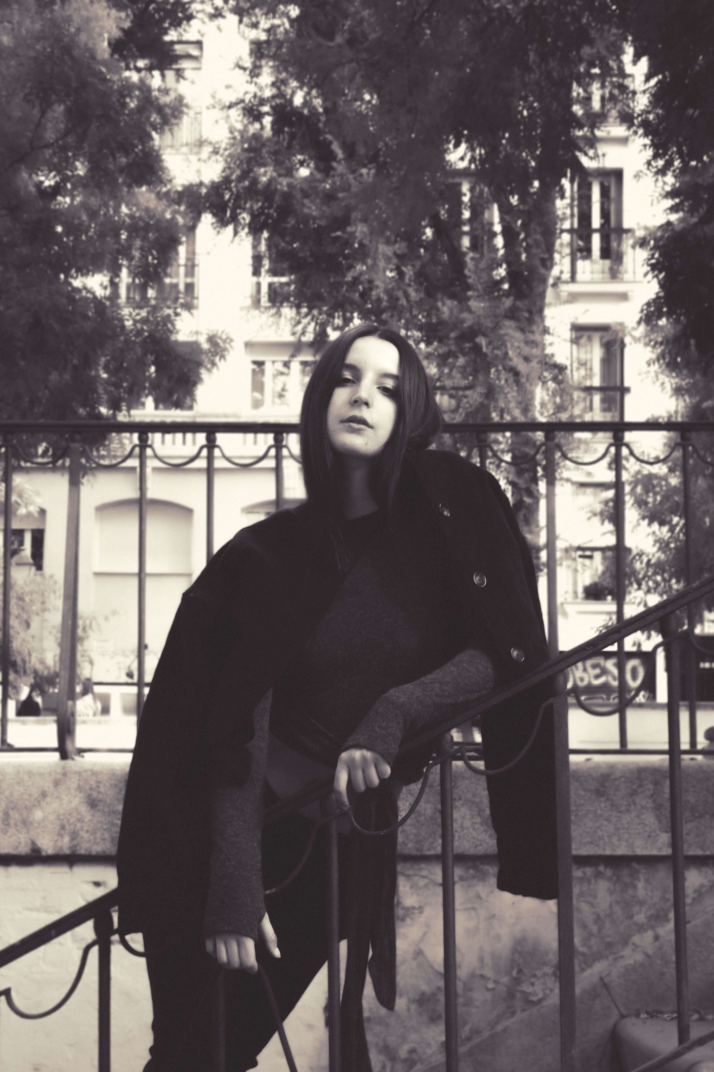 Woman in black jacket and grey top, posing confidently on a staircase outdoors