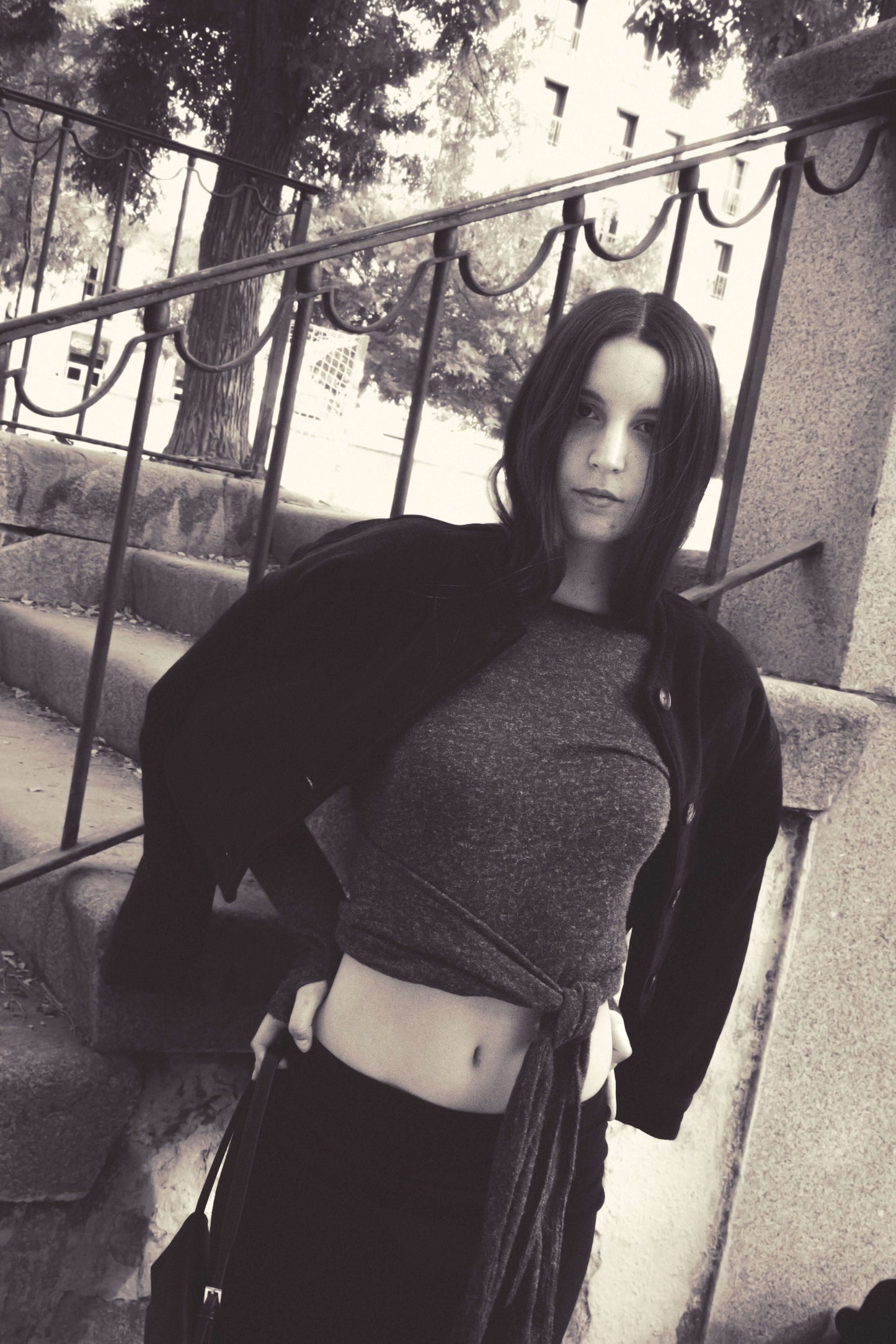 Fashionable woman in casual outfit with a tied grey top and black jacket, posing outdoors