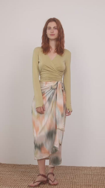 Cupro Multiway Wrap Top in Soft Olive worn with a vibrant tie-dye skirt, showcasing versatile styling options.