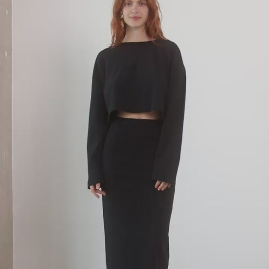Model wearing Organic Cotton Long Sleeve Top in Black with matching black skirt, standing against a neutral backdrop.