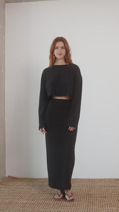 Model wearing Organic Cotton Long Sleeve Top in Black with matching black skirt, standing against a neutral backdrop.